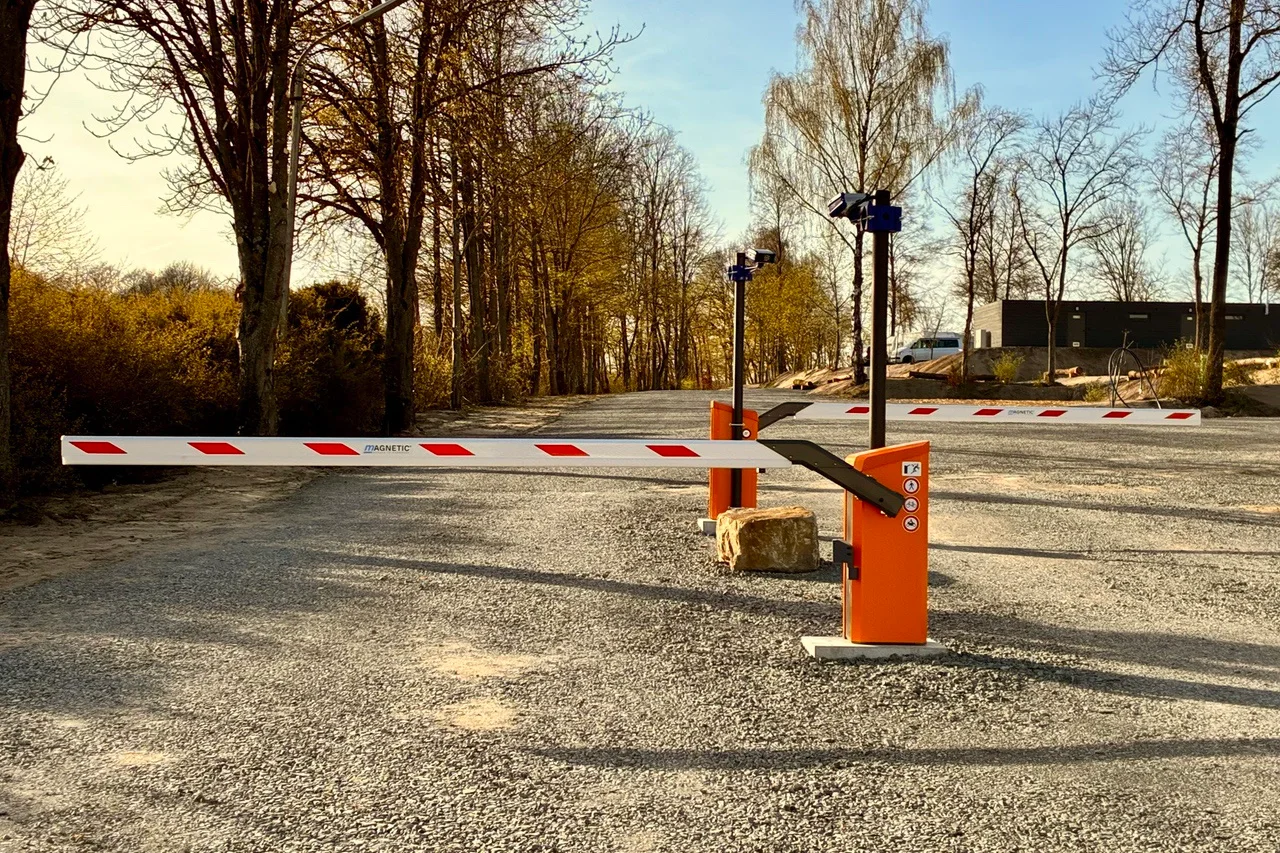 Entrance with two barriers on fresh gravel, the sanitary building behind