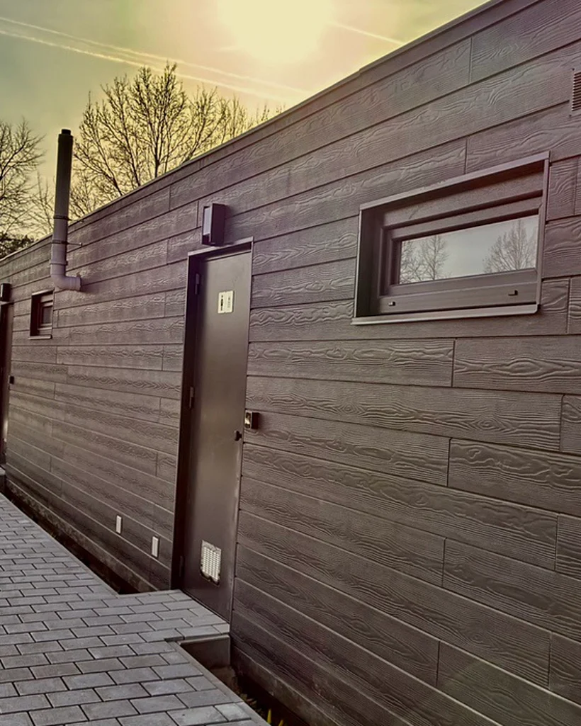 Eingang des Sanitärgebäudes mit Holzstruktur-Fassade und gepflastertem Weg