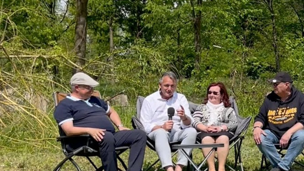 Still from the womoclick report: a group talking in camping chairs, one of them holding a microphone